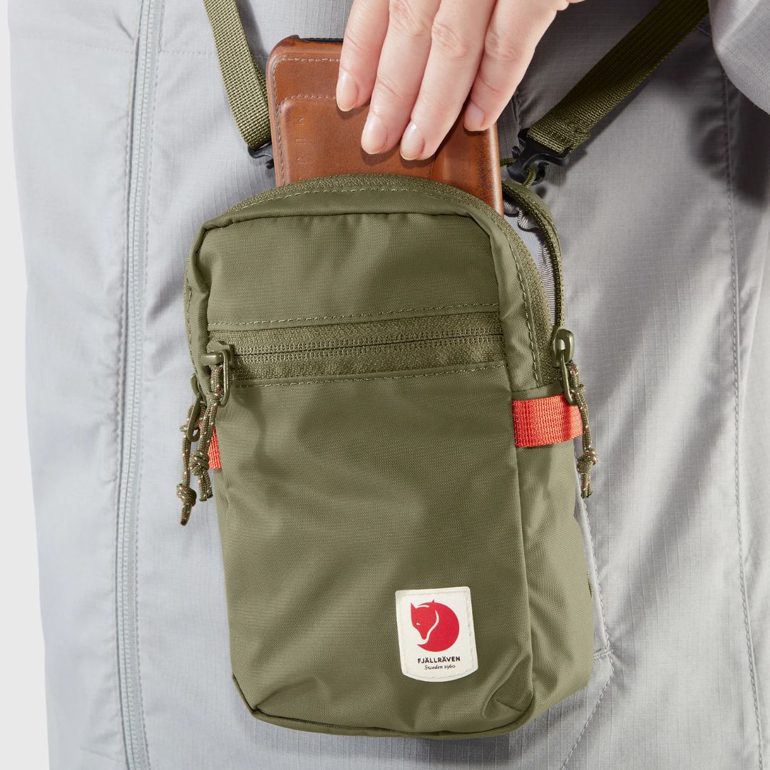 Persona guardando un móvil en el compartimento principal del bolso Fjällräven High Coast Pocket con cremallera.