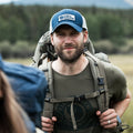 Primer plano de hombre con gorra Fjällräven Långtradarkeps y mochila en ruta de senderismo.
