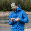 Hombre con gorra Fjällräven Långtradarkeps ajustando equipo de pesca en entorno natural.
