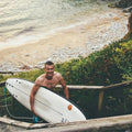 Surfista saliendo del agua con la tabla Flysurf Cold Hawaii 8.0 en un acceso a la playa.