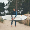 Surfista sujetando la tabla de surf Flysurf Cold Hawaii 8.0 en la playa con traje de neopreno.
