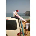 Surfistas colocando la tabla de surf rosa Flysurf Do It Your Wave 6.2 softboard en el techo de una furgoneta junto al mar.