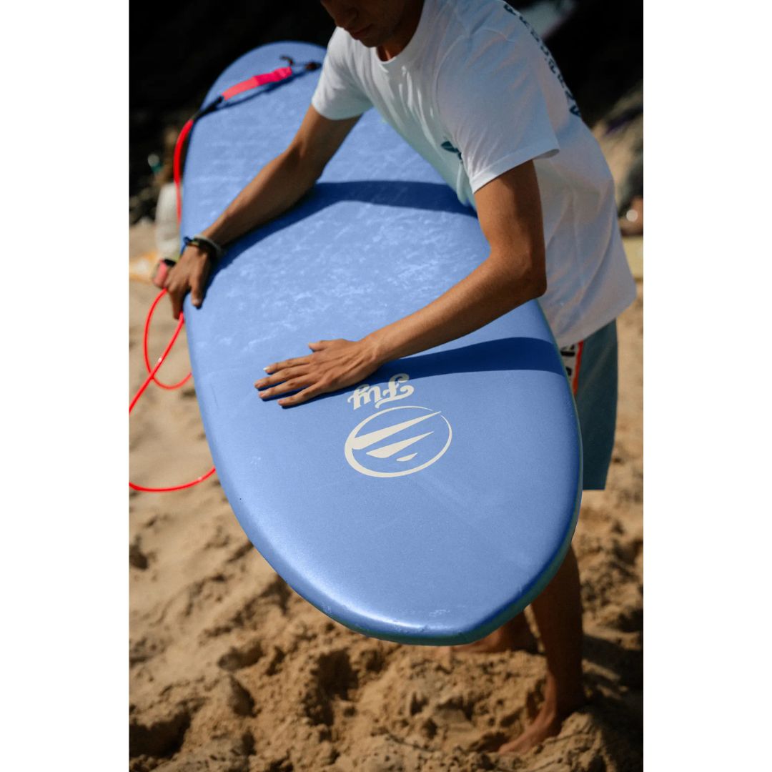 Tabla de surf softboard FLYSURF Do It Your Wave 6.4 Blue Wave en la playa, detalle del nose azul con logo Fly y leash rojo, tabla evolutiva para surfistas intermedios.