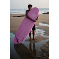 Surfista en la playa sosteniendo la tabla de surf rosa Flysurf Sea Calling 7.2 softboard para principiantes.