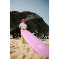 Surfista sujetando la tabla de surf rosa Flysurf Sea Calling 7.2 en la playa, tabla funboard blanda ideal para principiantes.
