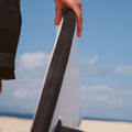 Surfista levantando la tabla de surf Flysurf The Traveller 6.6 blanca con logo Flysurf en la parte inferior.