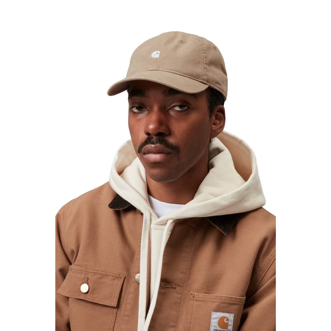 Carhartt WIP Madison Logo Cap en color leather con detalle blanco, vista frontal sobre modelo masculino. Gorra de seis paneles sin estructura en sarga prelavada negra con logo duck bordado en blanco, visera curva y hebilla metálica ajustable. Combinada con sudadera gris de cuello redondo con logo American Script de Carhartt WIP y cadena plateada.