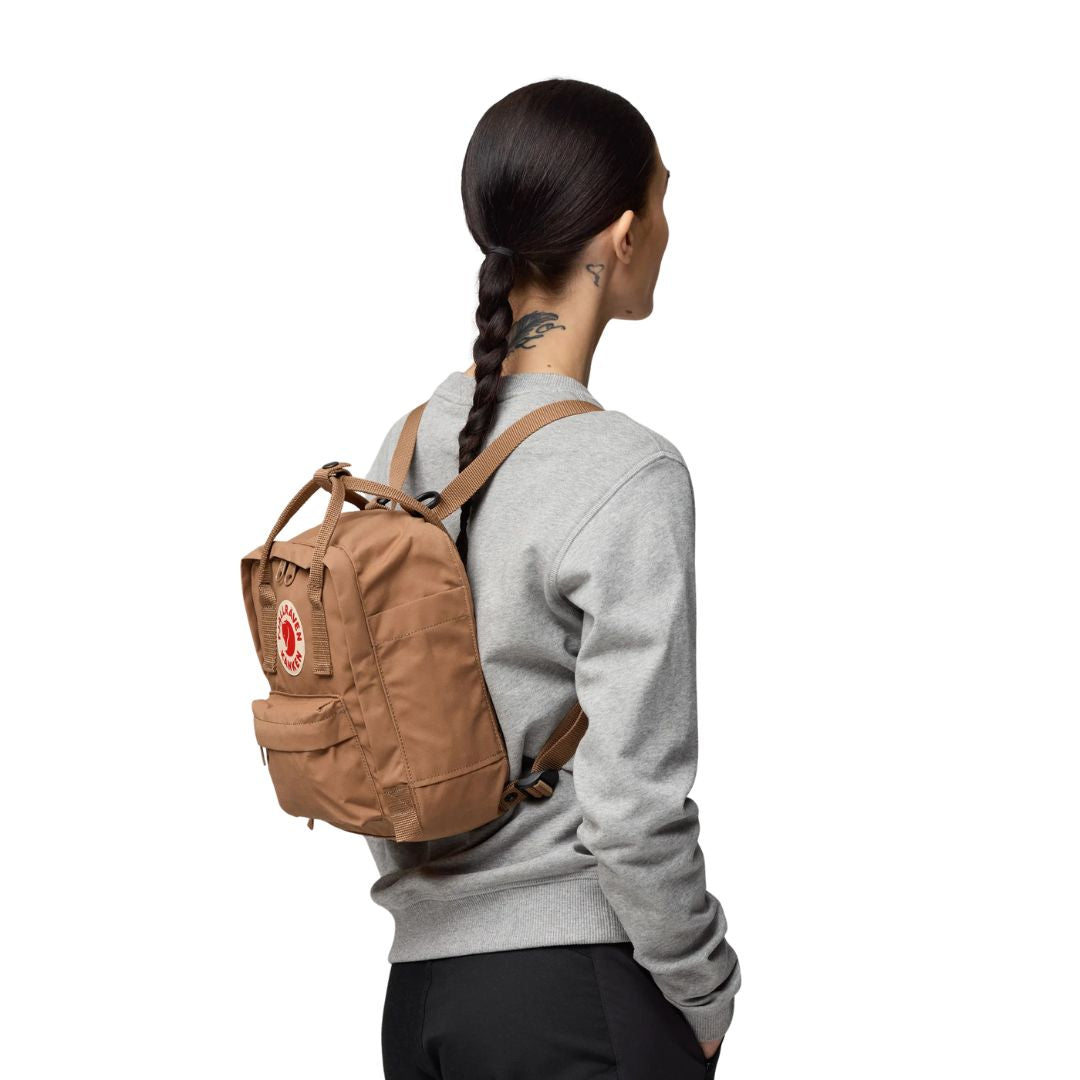 Mujer de perfil llevando mochila Fjällräven Kånken Mini color arena en la espalda, tirantes ajustados al cuerpo