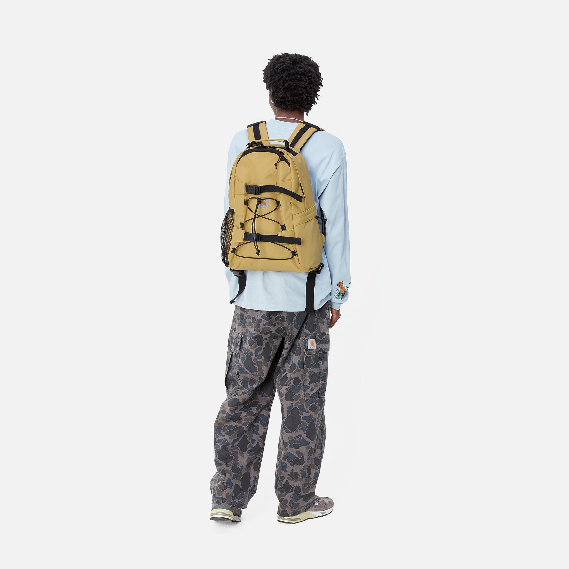 Modelo usando la mochila de skate impermeable Carhartt WIP Kickflip Backpack Bourbon, vista trasera mostrando el diseño funcional en uso.