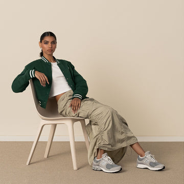 Modelo sentada llevando las zapatillas New Balance 2002R en color gris claro y azul marino, combinadas con un look casual.