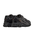 New Balance 1906R Grey Matter, vista par lateral posterior, upper de malla negra con overlays plateados, logo N negro y plateado y detalles en negro en suela.