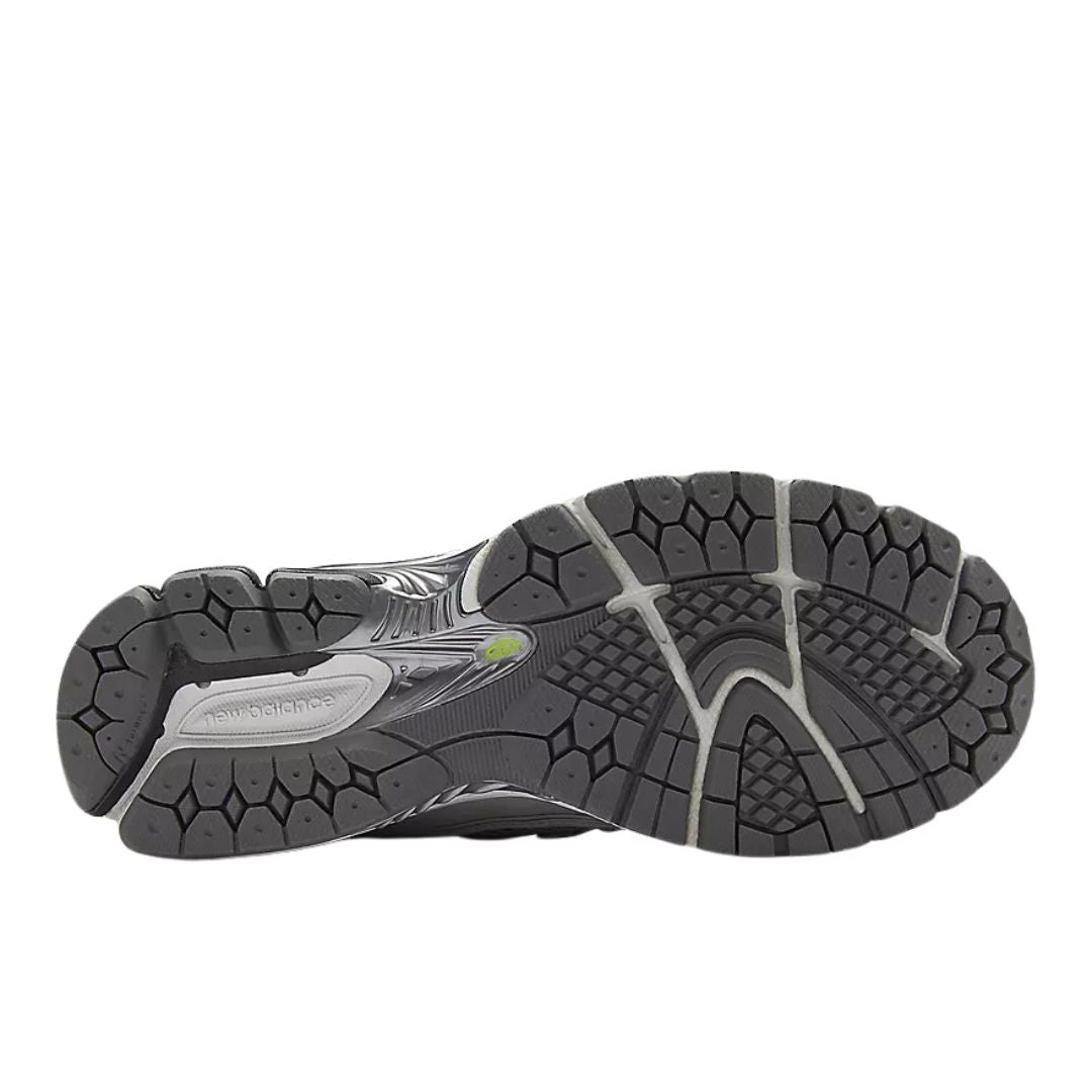 Suela de zapatillas New Balance 1906R en negro con patrón de tracción segmentado, diseño técnico para running y estabilidad, detalle central en gris y verde.