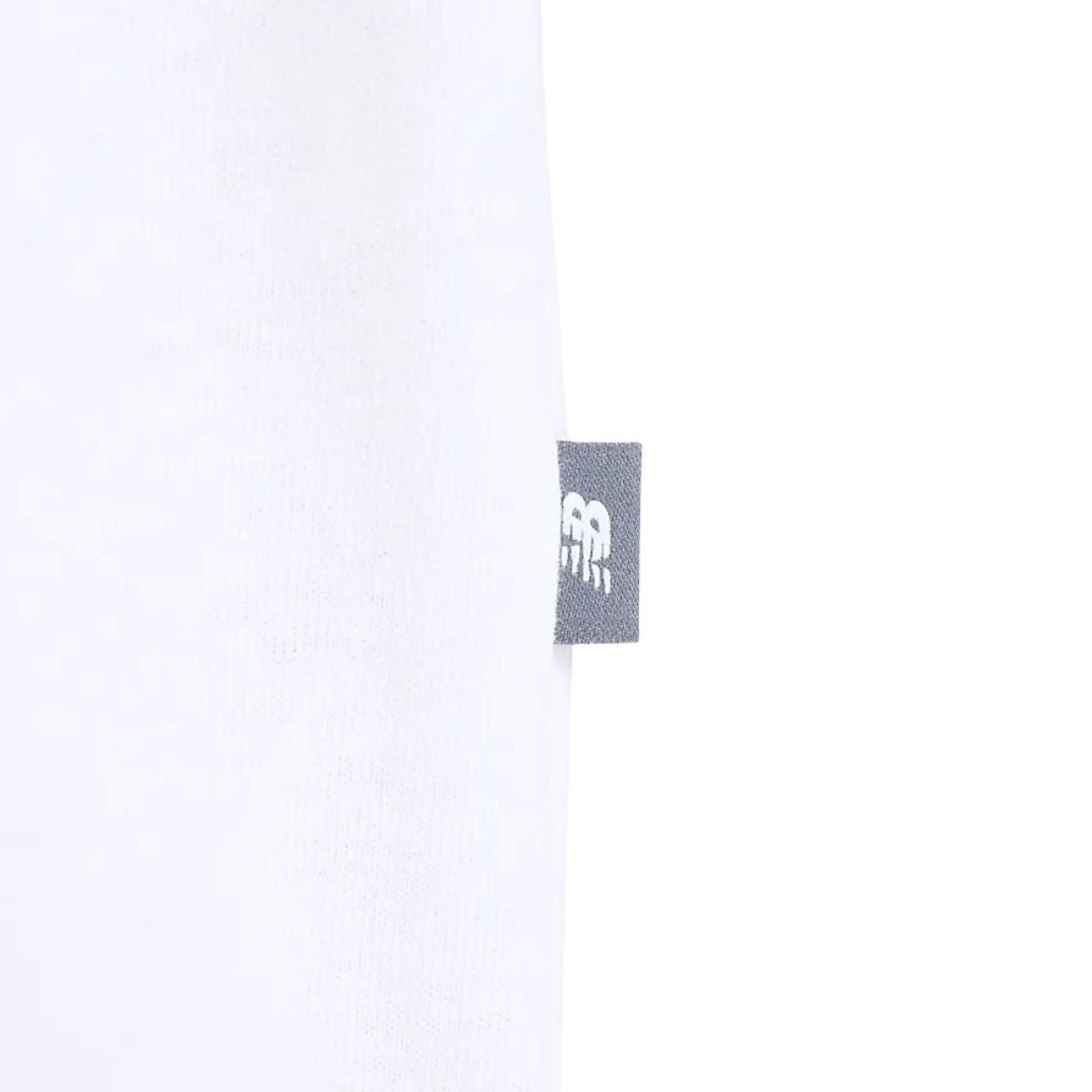 Detalle etiqueta lateral camiseta New Balance Fish and Chips blanca, con logo NB tejido en gris en el bajo izquierdo.
