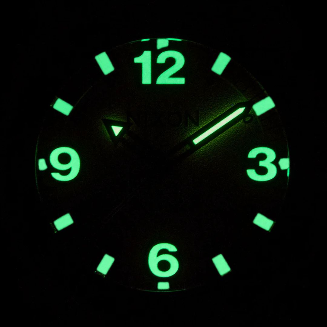 Esfera luminosa del reloj Nixon Clutch 42 Matte Gunmetal Hot Sauce con números y manecillas visibles en la oscuridad.