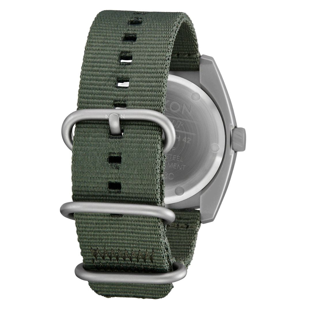 Detalle de la correa de nailon verde oliva del reloj Nixon Clutch 42 Matte Silver Thyme con hebillas metálicas.