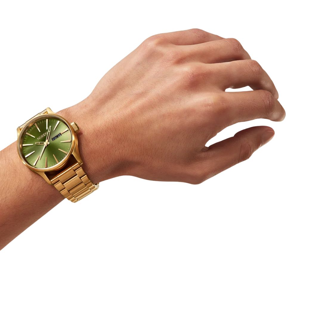 Reloj Nixon Sentry Stainless Steel dorado con esfera verde sunray en la muñeca de un modelo.