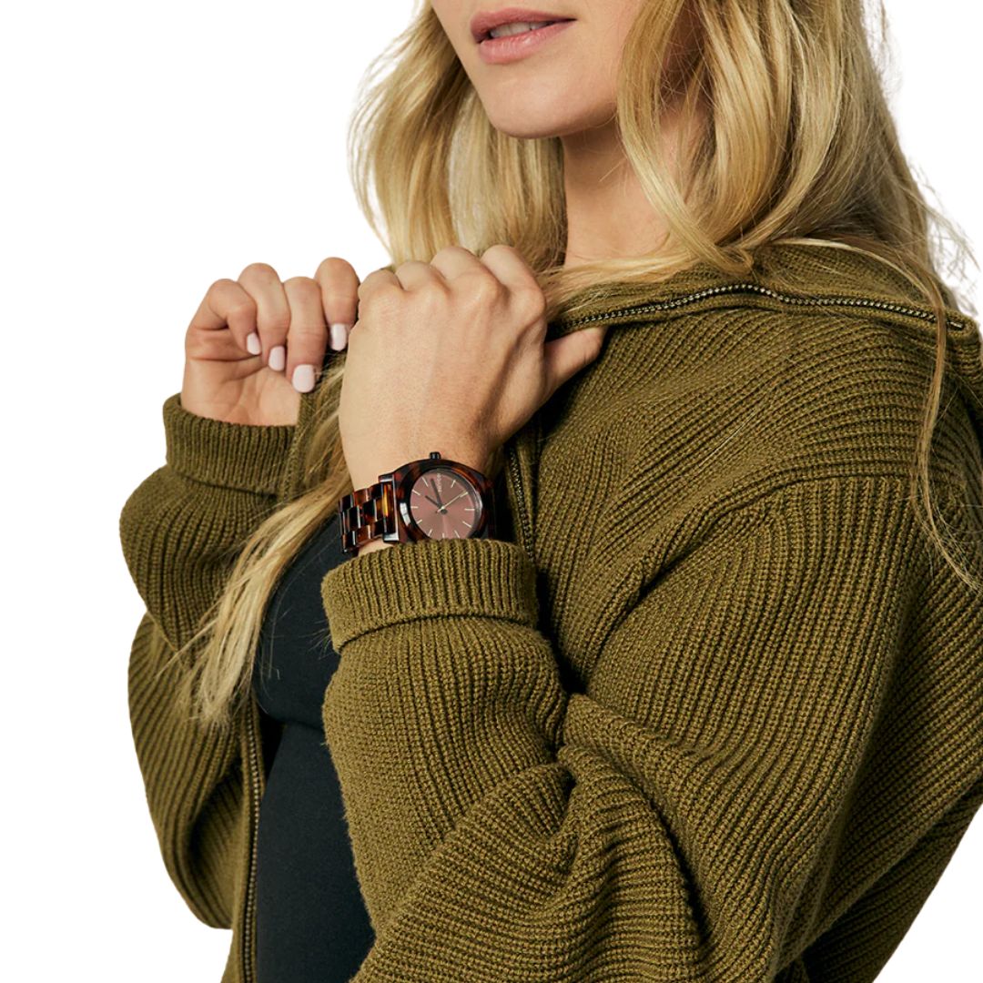 Reloj Nixon Time Teller Acetate tortoise oxblood en muñeca de mujer con suéter verde.