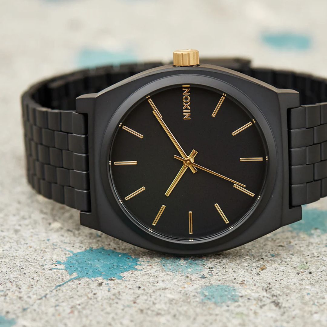 Primer plano del Nixon Time Teller All Matte Black Gold con índices y agujas doradas sobre esfera negra mate.