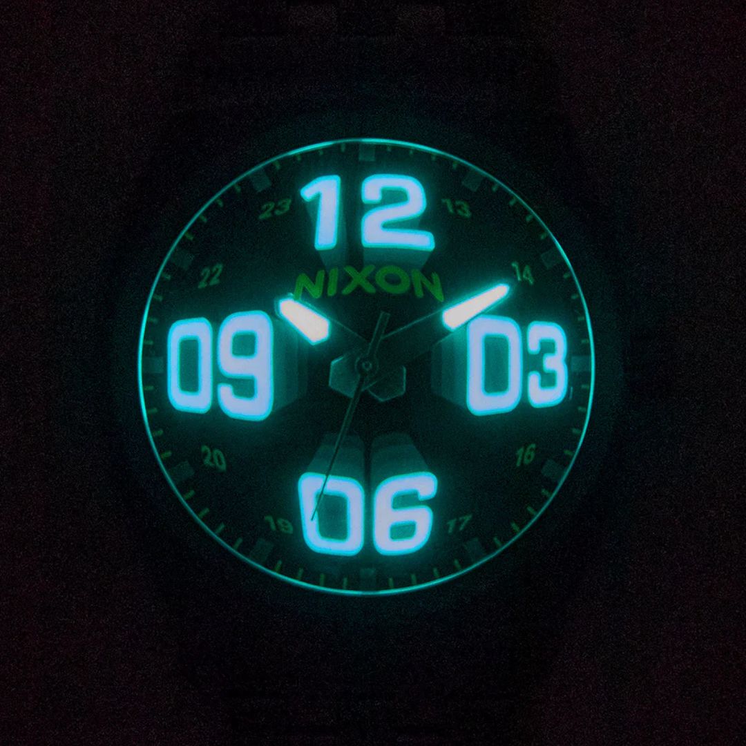 Esfera luminosa del reloj Nixon Time Teller Fisheye plateado con números grandes visibles en la oscuridad.