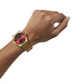 Reloj Nixon Time Teller dorado con esfera rojo oxblood sunray en muñeca masculina.