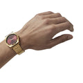 Reloj Nixon Time Teller dorado con esfera rojo oxblood sunray en muñeca femenina.
