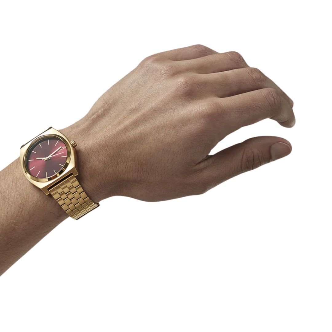 Reloj Nixon Time Teller dorado con esfera rojo oxblood sunray en muñeca femenina.