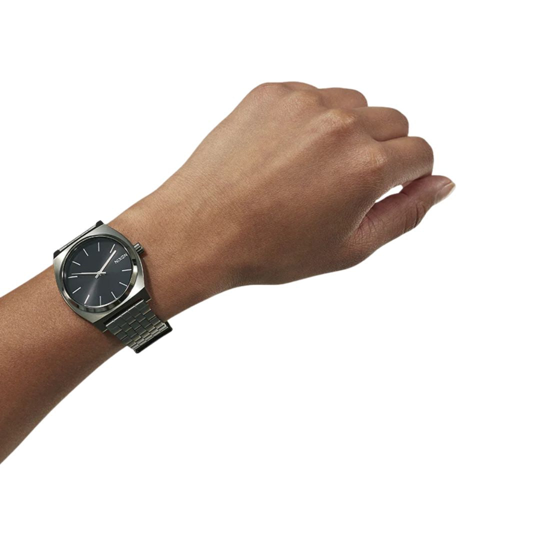 Reloj Nixon Time Teller Gunmetal Black Sunray en la muñeca de una persona, con esfera negra y correa gris metálica.