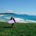 Surfista caminando hacia el mar con una tabla de surf softboard Ocean & Earth Happy Hour Epoxy Soft bajo el brazo, escena en costa australiana.