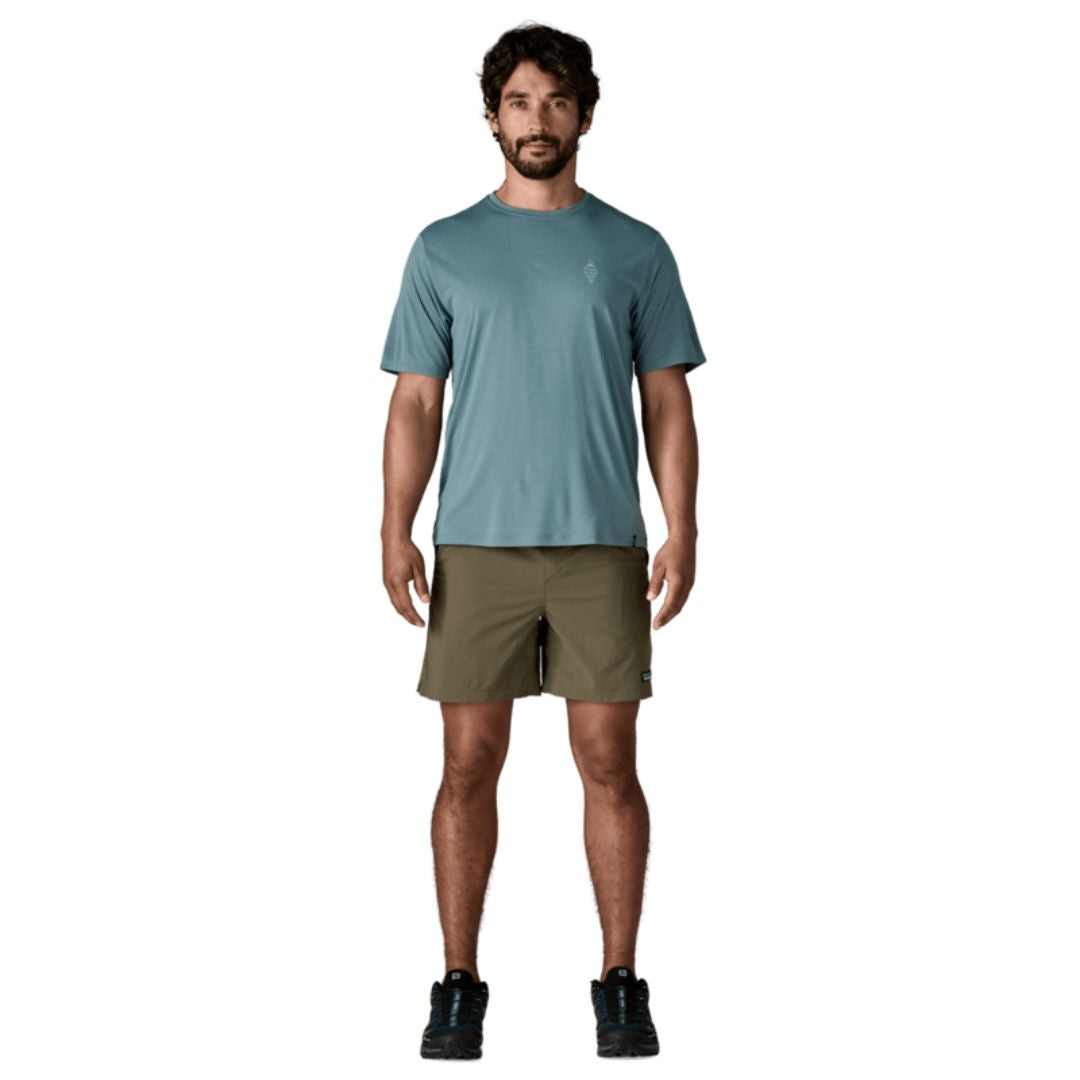 Hombre con Patagonia Baggies™ Lights 6" Basin Green de cuerpo entero: shorts slim fit verde oliva combinados con camiseta técnica azul y zapatillas de trail negras.