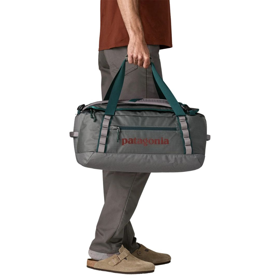 Patagonia Black Hole Duffel 40L color Noble Grey como bolsa de mano: asas reforzadas verde azulado, bolsillo exterior con cremallera y logo Patagonia rojo.
