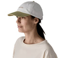 Patagonia Fitz Roy Icon Trad Cap en color blanco Birch White con visera verde Gumtree Green — vista trasera con tira ajustable de tela y etiqueta Patagonia visibles, llevada por una mujer con coleta.