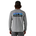 Vista trasera de hombre con camiseta Patagonia L/S P‑6 Logo Responsibili‑Tee en color Gravel Heather, con diseño gráfico del logo a gran escala.