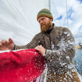 Chaqueta polar Patagonia Better Sweater en gris topo, hombre a bordo de un velero retirando hielo de una vela, con el cuello alto y la cremallera de pecho bien visibles sobre la prenda.