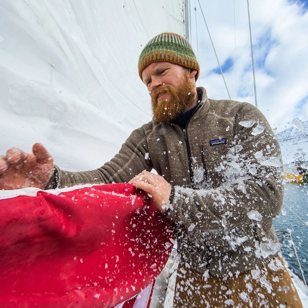Chaqueta polar Patagonia Better Sweater en gris topo, hombre a bordo de un velero retirando hielo de una vela, con el cuello alto y la cremallera de pecho bien visibles sobre la prenda.