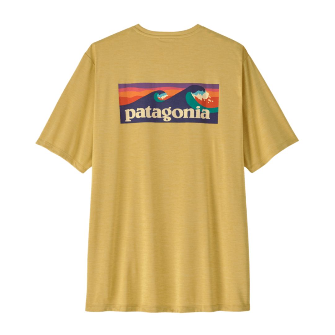 Patagonia Men's Capilene Cool Daily Shirt Boardshort Logo en color limestone yellow, vista trasera de producto plano sin modelo, mostrando el estampado completo Boardshort Logo con olas de surf en tonos verde petróleo y crema enmarcadas en rectángulo sobre fondo verde azulado jaspeado.