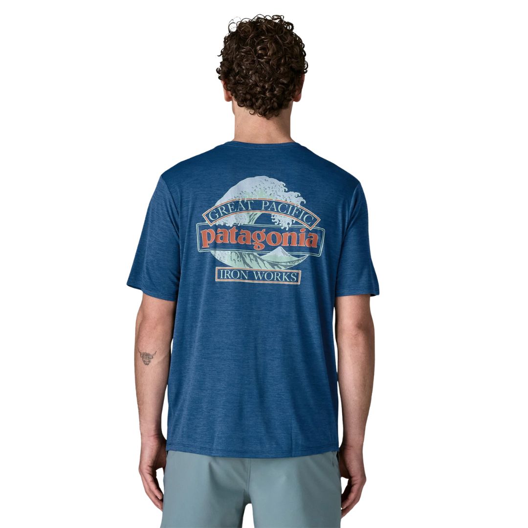 Patagonia Men's Capilene Cool Daily Shirt Great Waves en color clement blue light clement blue x-dye, vista trasera con modelo, mostrando el estampado Great Pacific Patagonia Iron Works con ola de Hokusai en tonos menta y coral sobre fondo azul.
