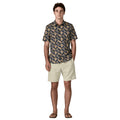 Patagonia Men's Go-To Shirt en estampado jaguar geo dolomite blue, vista frontal completa con modelo combinada con pantalón corto beige arena y chanclas marrones, mostrando el corte slim fit, el estampado geométrico de triángulos con motivos de palmeras y jaguares en azul marino y beige, el bolsillo izquierdo del pecho y el bajo redondeado por fuera del pantalón.