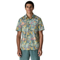 Patagonia Men's Go-To Shirt en estampado moon tripper blue sage, vista frontal con modelo combinada con pantalón corto verde azulado, mostrando el cuello con solapas, la tapeta de botones, el bolsillo izquierdo del pecho y el estampado tropical de figuras lunares y hojas en tonos verde azulado, amarillo mostaza y rosa sobre tejido ligero de algodón orgánico y poliéster reciclado.