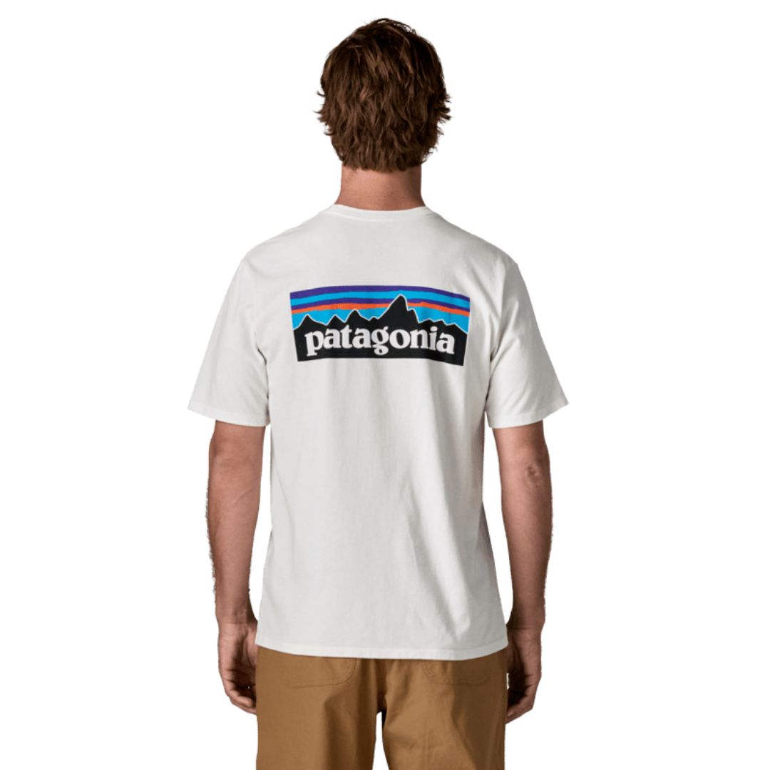 Camiseta Patagonia P-6 Logo Responsibili-Tee en color blanco (Fiber White), modelo visto de espaldas mostrando el icónico logotipo P-6 con las montañas y el degradado de colores.
