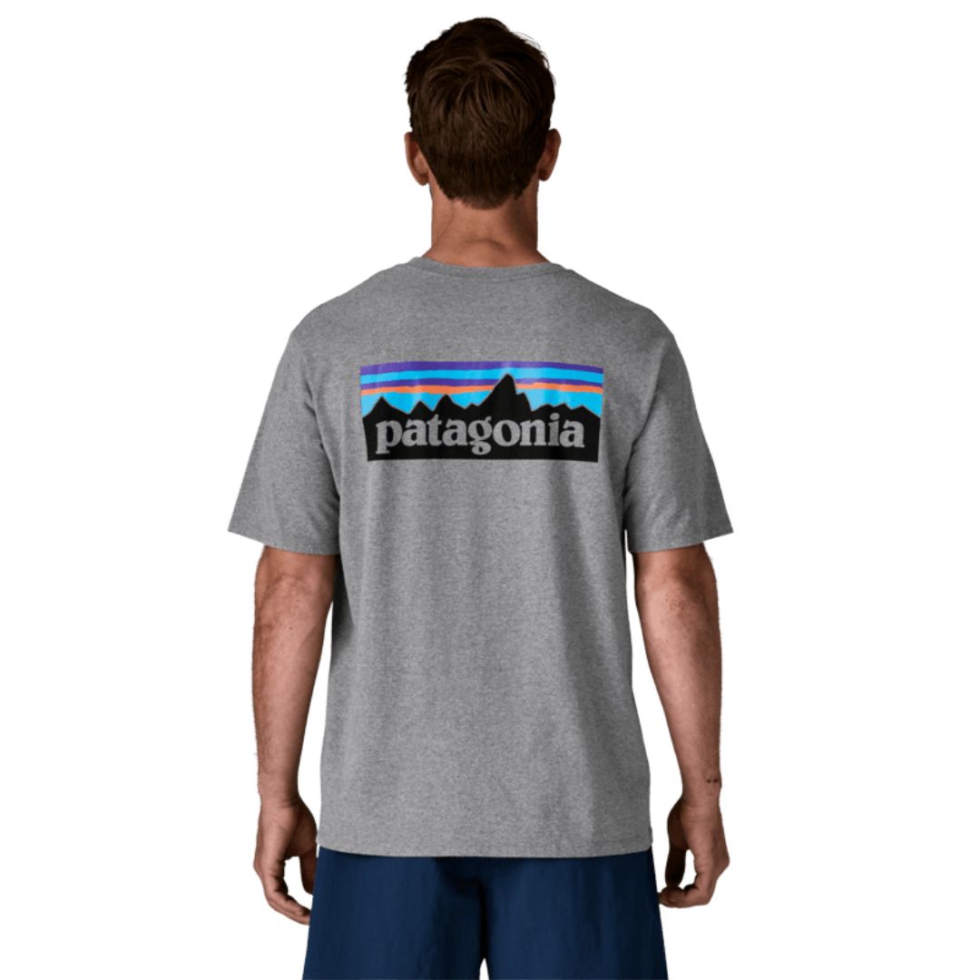 Camiseta Patagonia P-6 Logo Responsibili-Tee en color gris jaspeado (Gravel Heather), modelo visto de espaldas mostrando el icónico logotipo P-6 con las montañas y el degradado de colores.