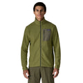 Patagonia Men's R1 Air Fleece Jacket en color caper green, vista frontal con modelo, cremallera completa cerrada, cuello alto, bolsillo pectoral izquierdo con panel en tejido liso verde oliva, cremallera con tirador y etiqueta Patagonia visible.