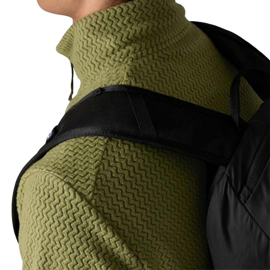 Patagonia Men's R1 Air Fleece Jacket en color caper green, detalle de las costuras off-shoulder descentradas con correa de mochila negra sobre el hombro, demostrando la comodidad de uso con mochila y el tejido jacquard en zigzag de poliéster reciclado.