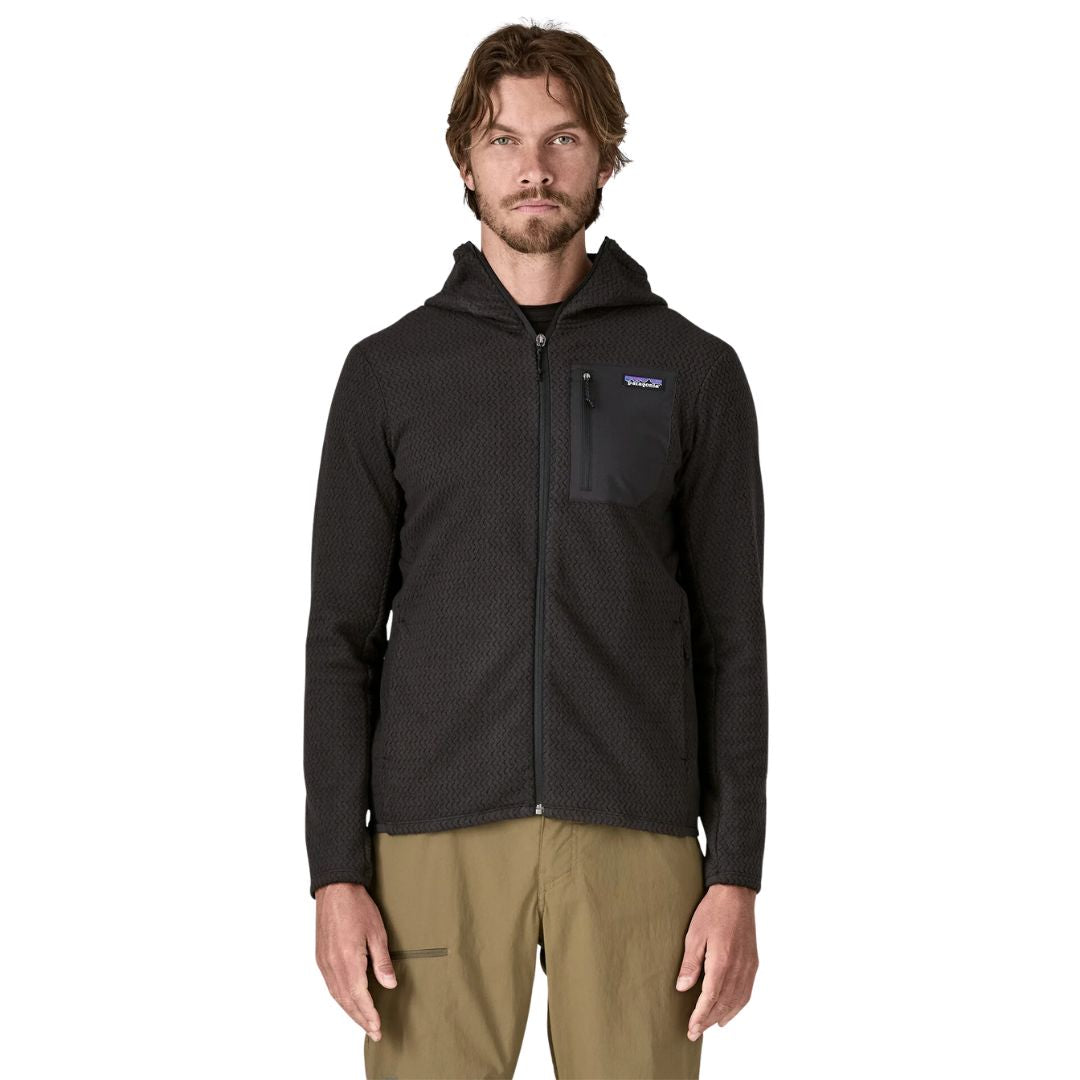 Patagonia Men's R1 Air Full-Zip Hoody en color negro, vista frontal con modelo, capucha baja sobre los hombros, cremallera completa abierta, bolsillo pectoral izquierdo con panel en tejido liso y etiqueta Patagonia en azul y morado.