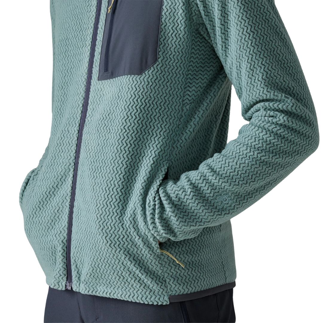 Patagonia Men's R1 Air Full-Zip Hoody, detalle lateral del bajo y la manga, mostrando el tejido jacquard en zigzag de poliéster reciclado, el ribete tejido en el bajo y el bolsillo delantero con cremallera minimalista.
