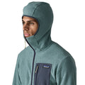 Patagonia Men's R1 Air Full-Zip Hoody con capucha slim-fit subida, mostrando el ajuste ceñido alrededor del rostro, tejido jacquard en zigzag, cremallera completa y bolsillo pectoral con etiqueta Patagonia.
