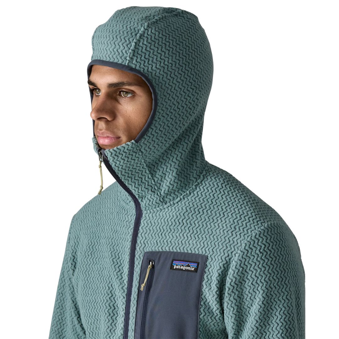 Patagonia Men's R1 Air Full-Zip Hoody con capucha slim-fit subida, mostrando el ajuste ceñido alrededor del rostro, tejido jacquard en zigzag, cremallera completa y bolsillo pectoral con etiqueta Patagonia.