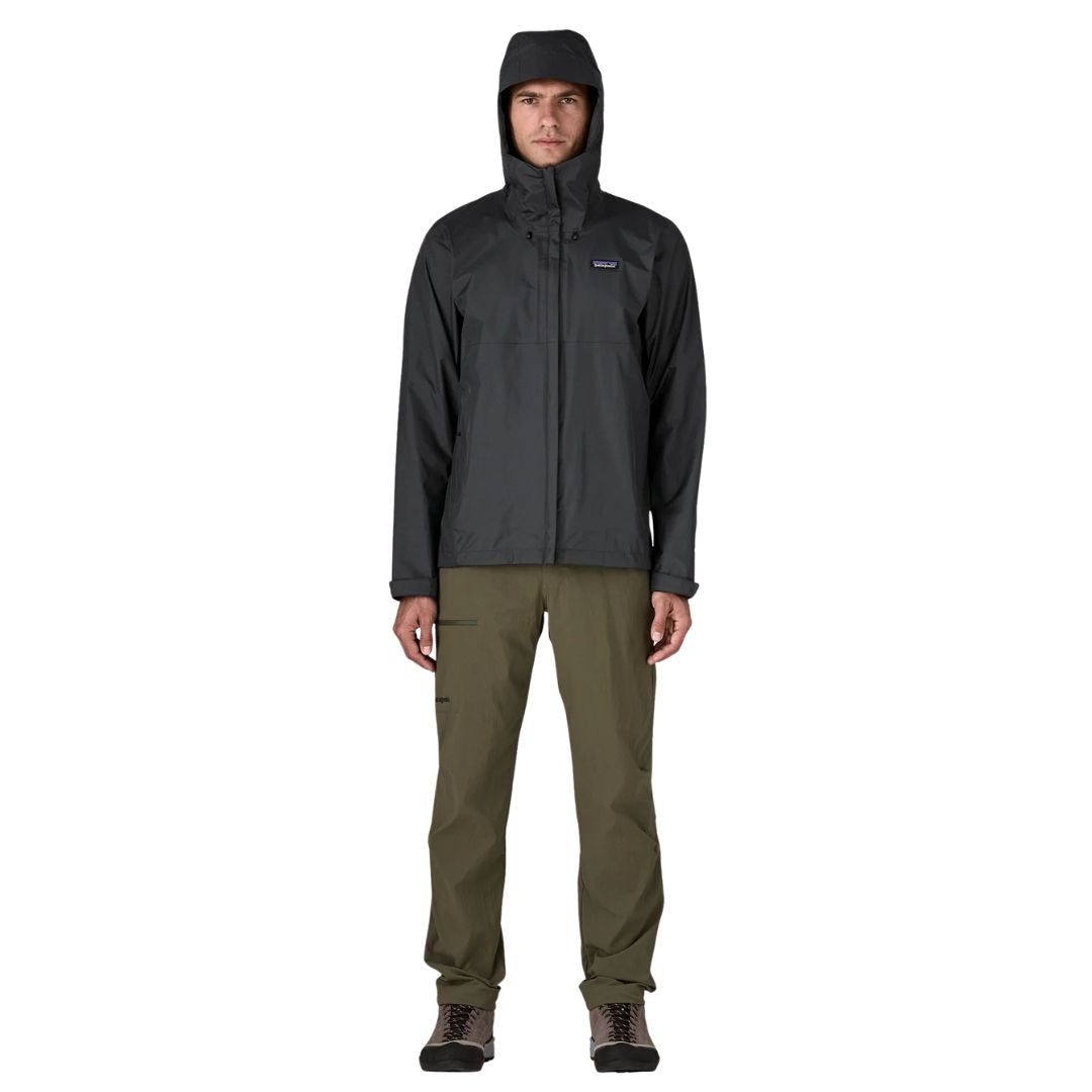 Patagonia Torrentshell 3L color negro, cuerpo completo en modelo con capucha puesta, cremallera central antiintemperie, parche logo P-6 y regular fit para senderismo.