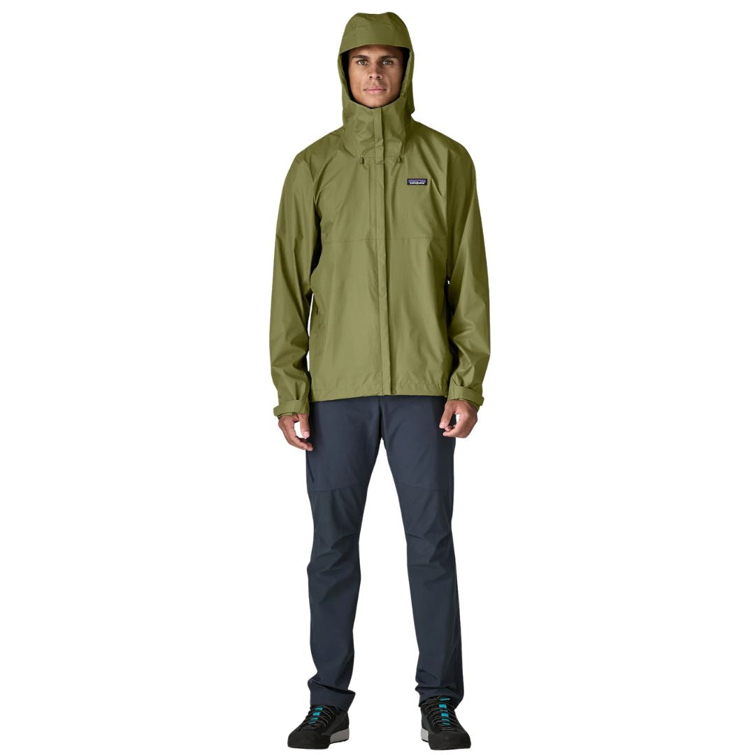 Patagonia Torrentshell 3L color Caper Green, cuerpo completo en modelo con capucha puesta, cremallera central antiintemperie, parche logo P-6 y regular fit.
