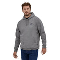 Sudadera con capucha Patagonia P-6 Label Uprisal Hoody en gris Gravel Heather, vista frontal en ángulo sobre modelo, con capucha, cordón y etiqueta Patagonia en el pecho.