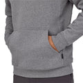 Detalle del bolsillo canguro de la sudadera Patagonia P-6 Label Uprisal Hoody en gris Gravel Heather, mostrado sobre modelo con la mano dentro y bolsillo lateral con cremallera.